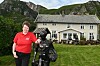 Malin i rød skjorte står ved en svart skulptur foran Klokkergården på Rødøya, med fjell bak.