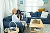 En kvinne sitter i en blå sofa med hunden Karla på fanget i en lys stue.