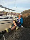Trude sitter på et svaberg ved en seilbåt og arbeider på en bærbar datamaskin.