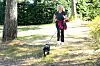 Trude Teige i svarte treningsklær går eller løper med den lille svarte hunden Karla i bånd på en skogssti.