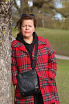 Else står ved et tre i en park, iført rød rutete kåpe og svart veske.