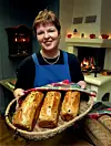 Wenche holder en flettet kurv med tre nystekte brød foran en tent peis i et TV-studio.