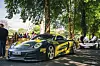 Gul og svart Porsche parkert på et biltreff, med folk og en hvit sportsbil i bakgrunnen.