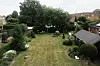 Oversiktsbilde av en velstelt hage med stor plen, blomsterbed, busker, trær og en overbygd sitteplass.