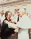 Pave Johannes Paul II håndhilser på Henning Madsen foran en monumental steinbygning i Vatikanet.