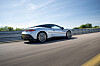 En sølvfarget Aston Martin Vantage kjører på en racerbane med autovern og trær i bakgrunnen.