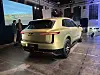 Lysegul Genesis-SUV sett bakfra på et innendørs arrangement, med presentasjonsskjerm i bakgrunnen.