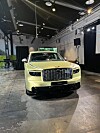 Lysegrønn Genesis SUV sett forfra i et industrielt utstillingslokale med spotlys i taket.