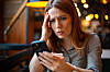Bekymret kvinne holder en smarttelefon og tar seg til pannen ved et kafébord.